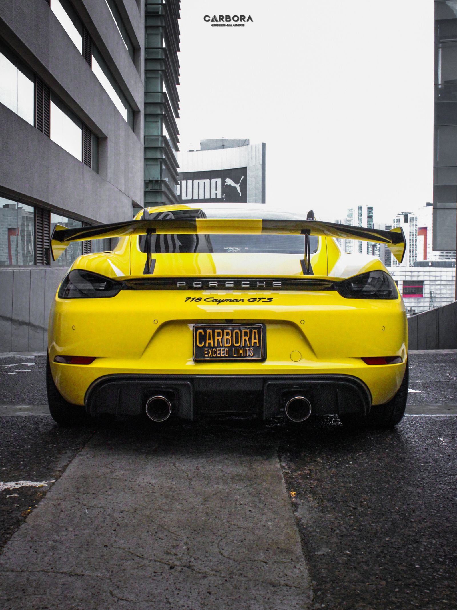 Porsche 718 Cayman GTS amarillo, visto por detrás, con el alerón tipo GT4 RS instalado y placa promocional CARBORA.