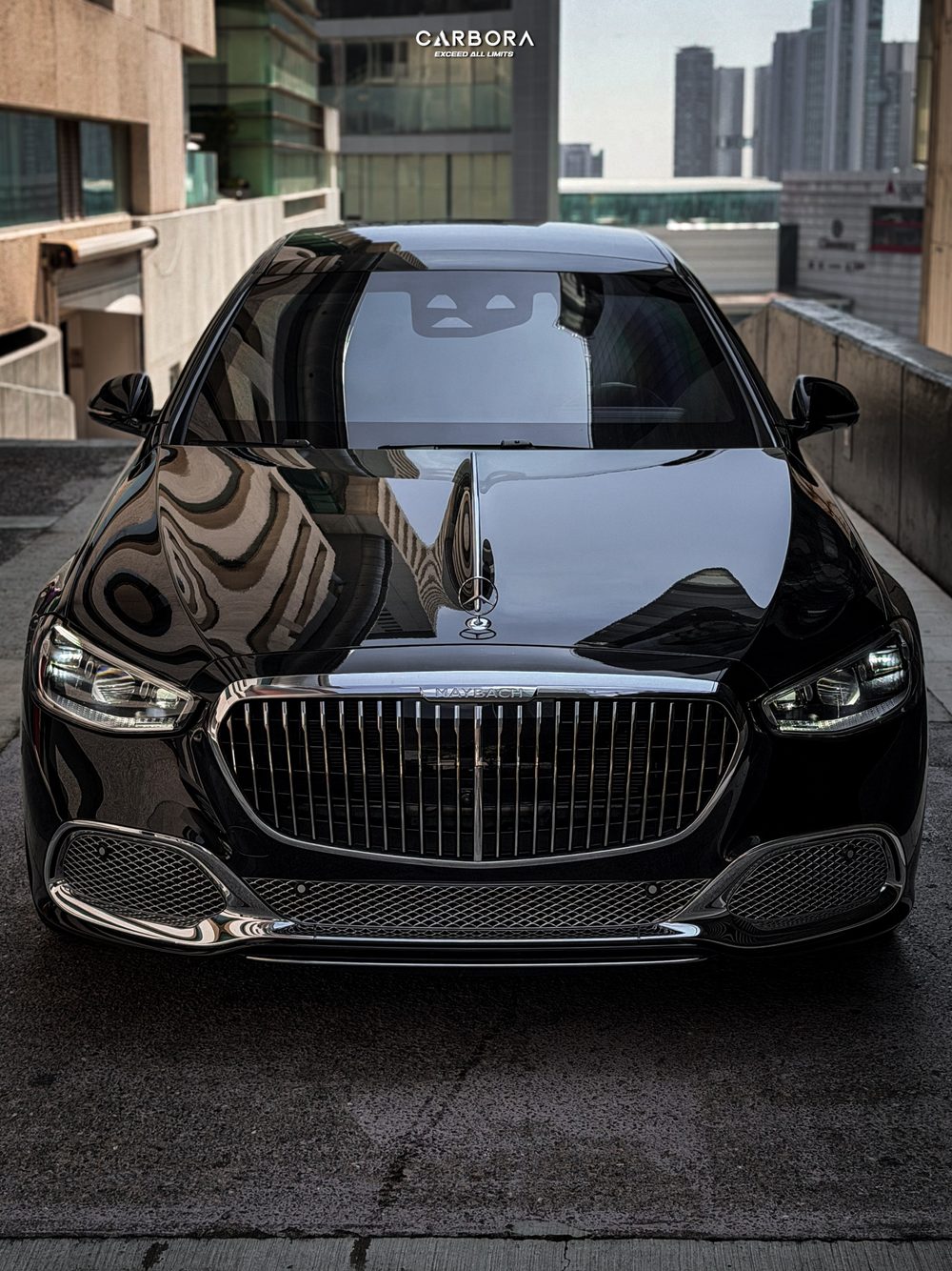 Vista frontal de un Mercedes-Maybach; el brillo de la carrocería refleja los edificios del entorno.