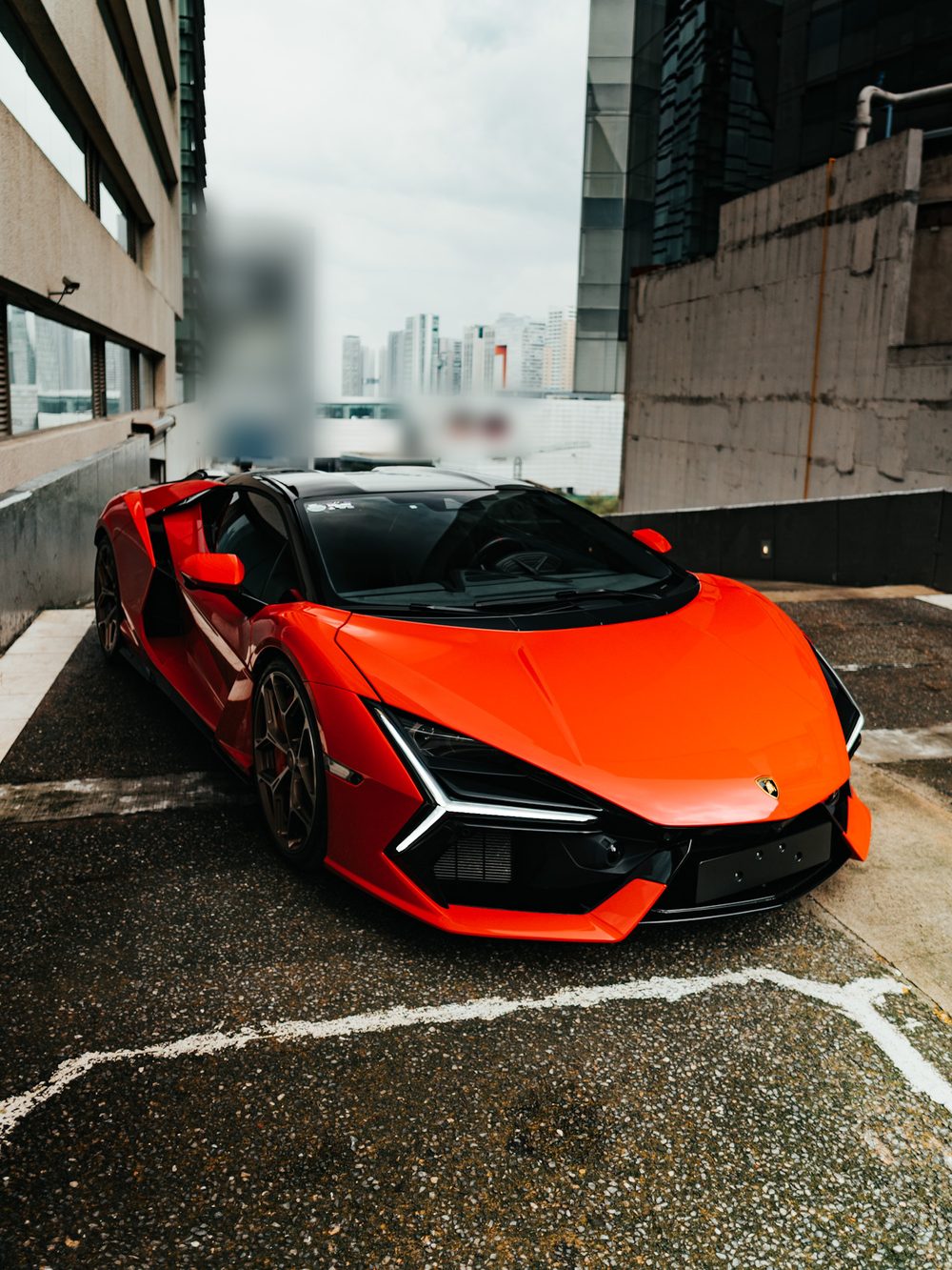 Lamborghini Revuelto en naranja intenso, tres cuartos frontal sobre una azotea de estacionamiento con las torres de Santa Fe al fondo.