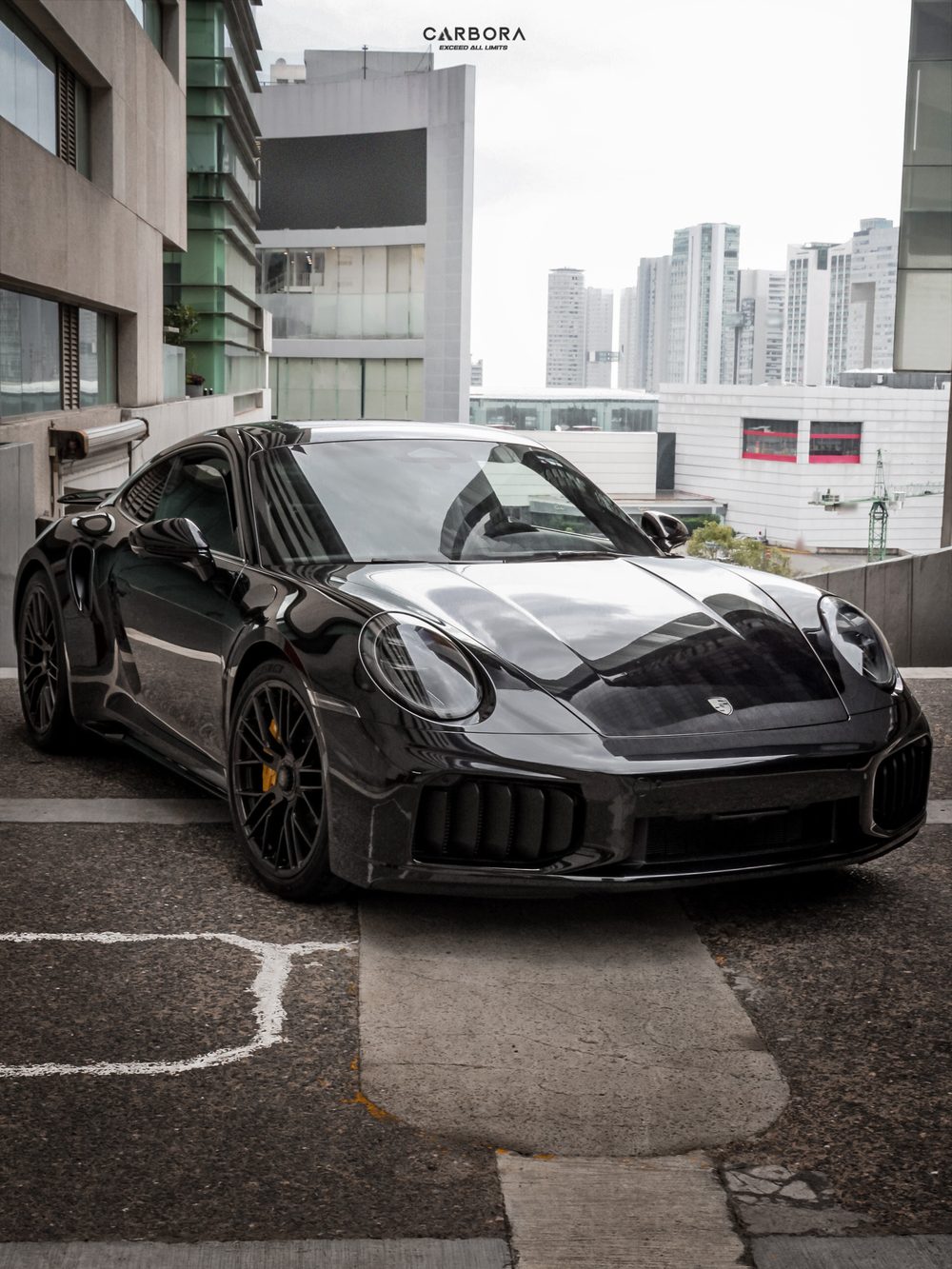 Porsche 911 Turbo 992.2 negro en tres cuartos frontal sobre una rampa de concreto, con las fachadas reflejándose limpias sobre el cofre y el costado.