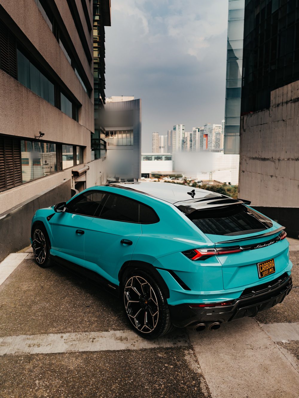 Lamborghini Urus turquesa, tres cuartos trasero desde un punto elevado, con el skyline de Santa Fe al fondo. Techo panorámico y alerón de fibra de carbono, rines oscuros y salidas de escape cuádruples.