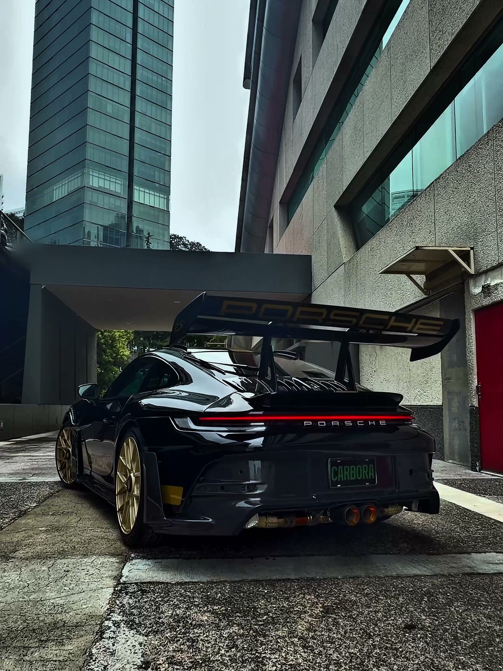 Porsche 911 Carrera S en configuración tipo GT3 RS, negro, visto en tres cuartos traseros: alerón tipo GT3 RS con soportes de cisne, rines dorados y salidas de escape centrales.
